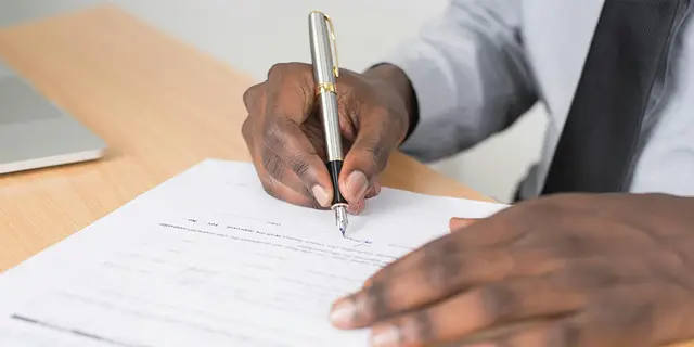 A person in a shirt and tie signing a property document with a fountain pen
